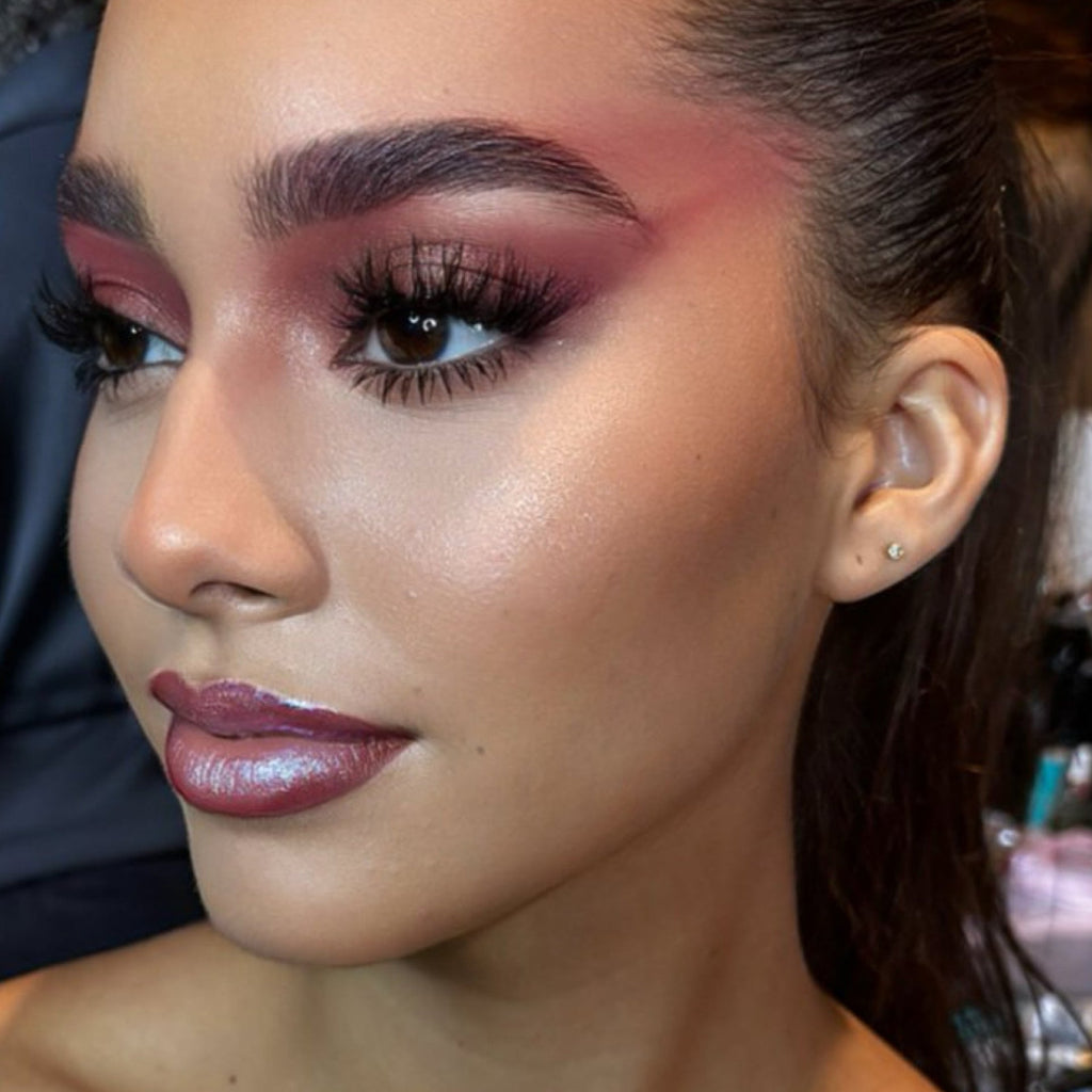 Close-up of woman's face with dramatic red and pink makeup, shiny lipstick, and stud earring.
