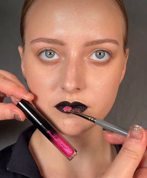 A woman applying pink glitter to her black lipstick with a brush.